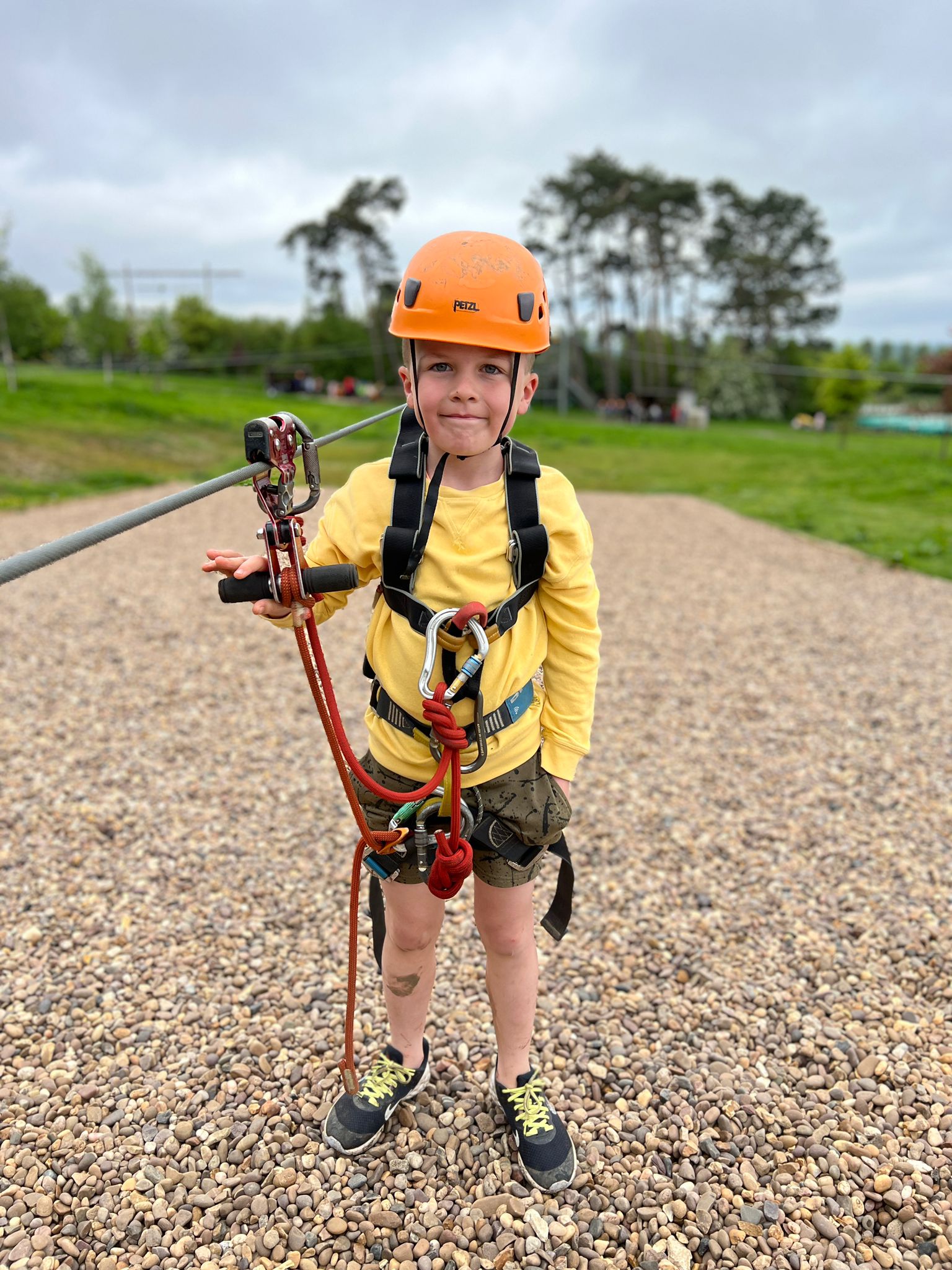 A boy stands at the bottom of the zip wire at PGL, he is wearing his harness and helmet and holding a rope.