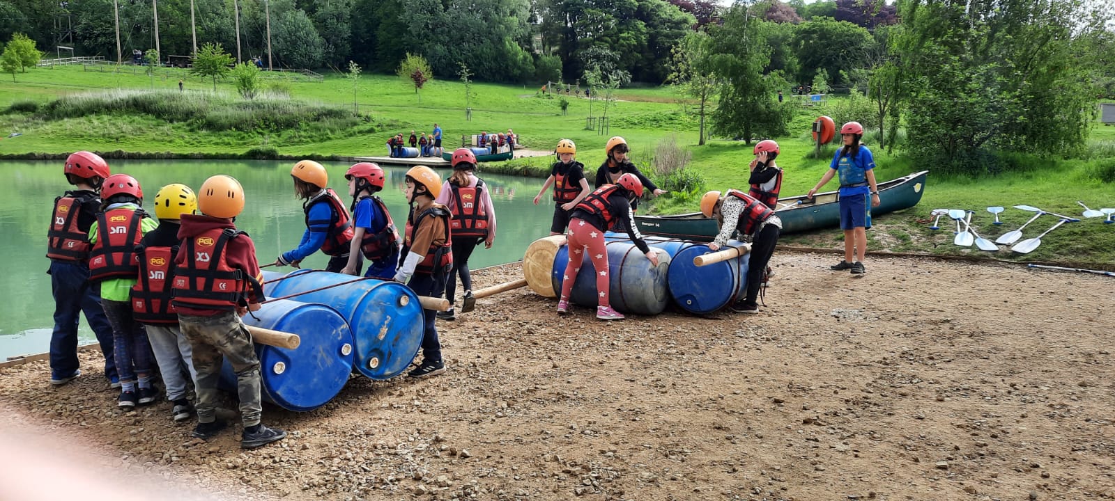 Children grouped next to a lake, preparing to launch rafts they have build using rope, wood and blue plastic bung drums