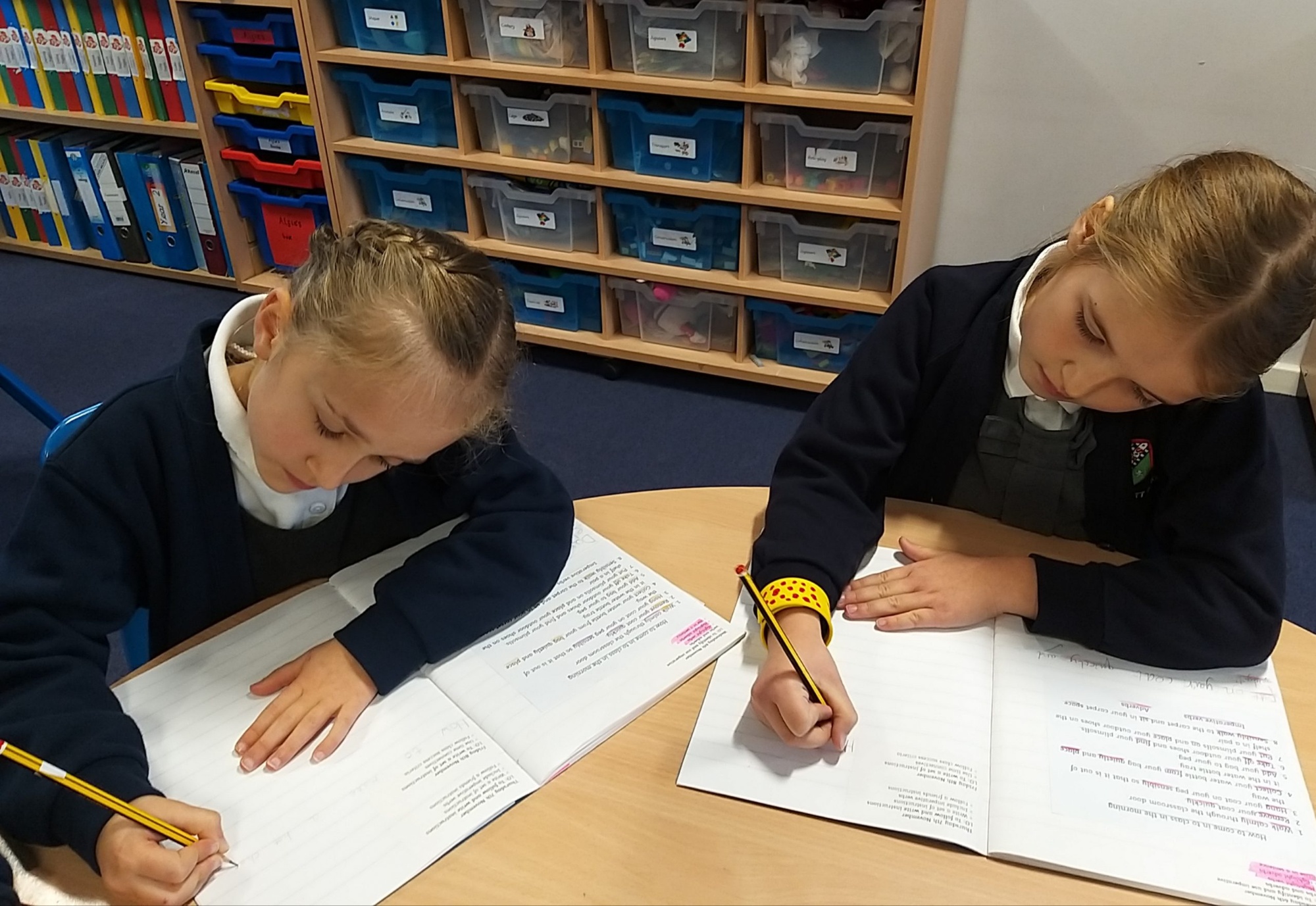 Two girls sit quietly at their table completing a writing task in their English books.