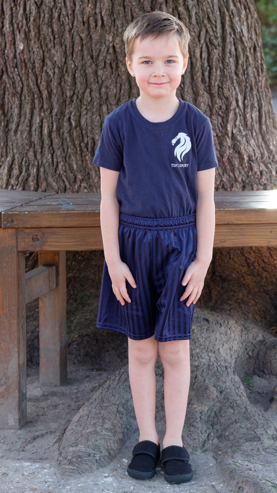 A male pupil stands outside wearing his outdoor PE kit, consisting of shorts and a school PE t-shirt