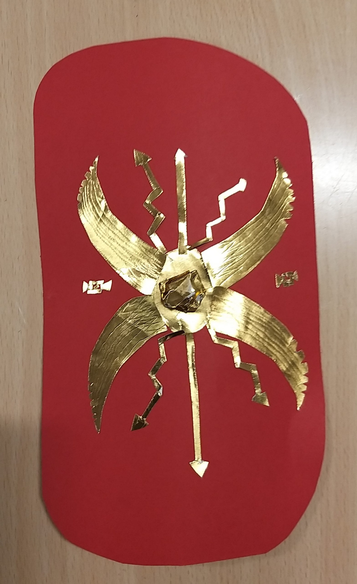 Roman shield, designed by a child, shows a detailed and decorative gold design on a red, oblong shaped shield.