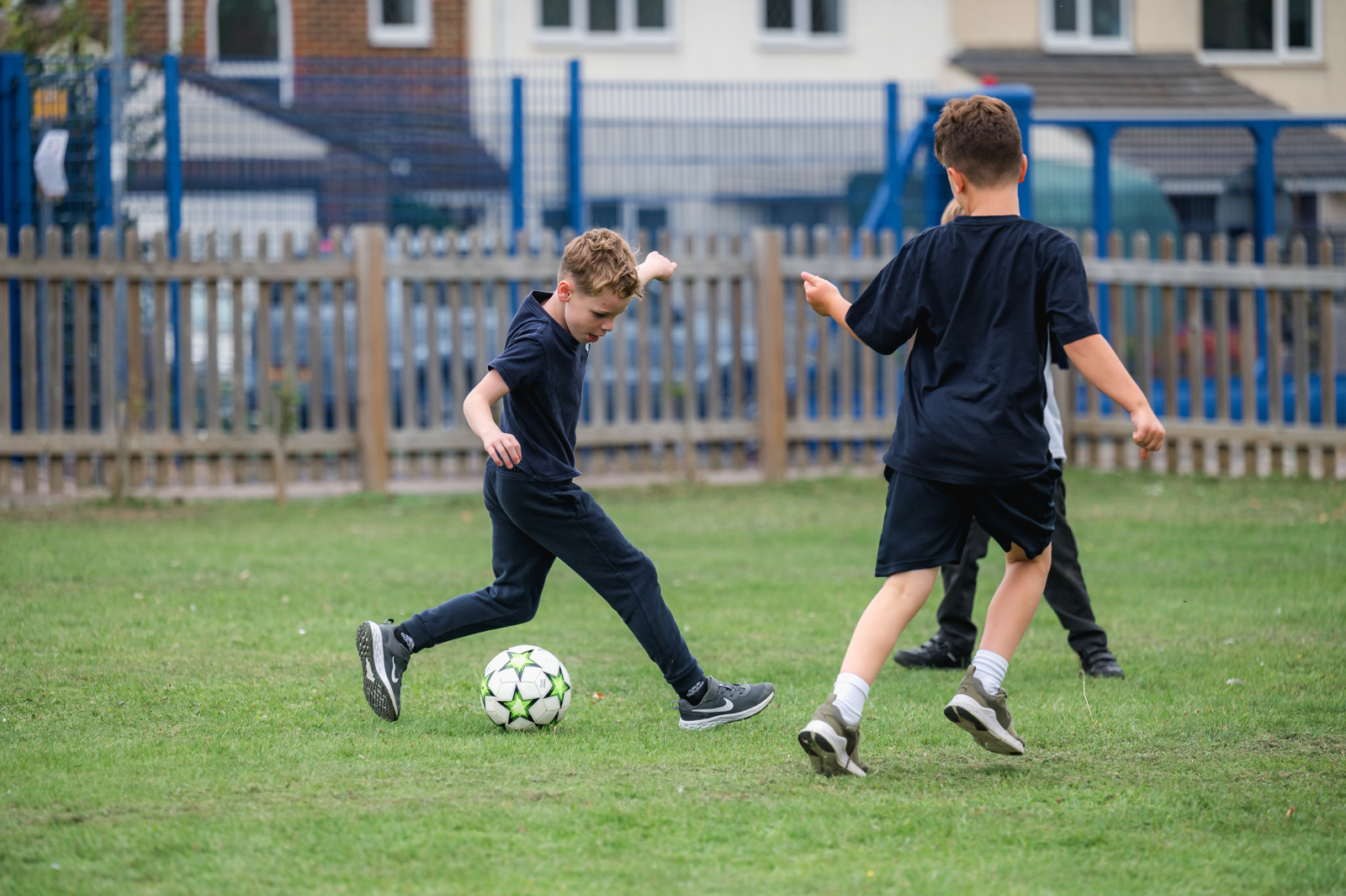 Three boys play a game of football on the school field, one of the boys is about to make a back pass to his team mate.