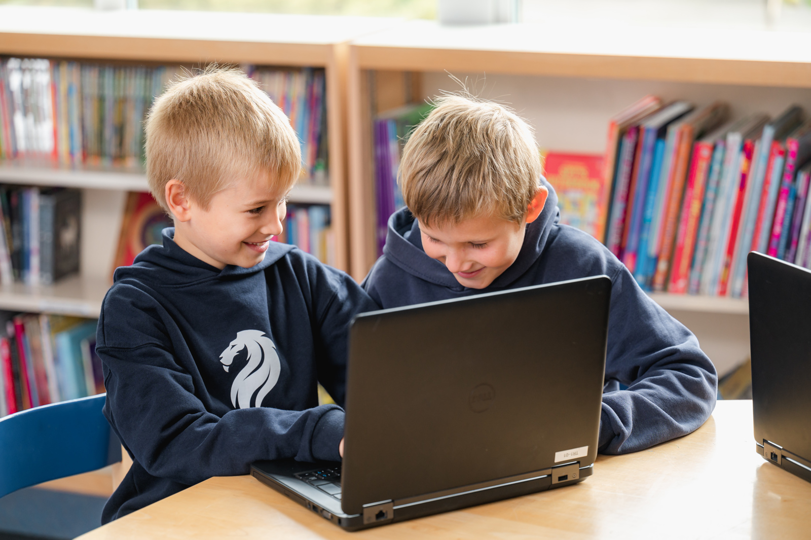 Two boys sit next to each other, sharing a laptop to complete an ICT learning task together.