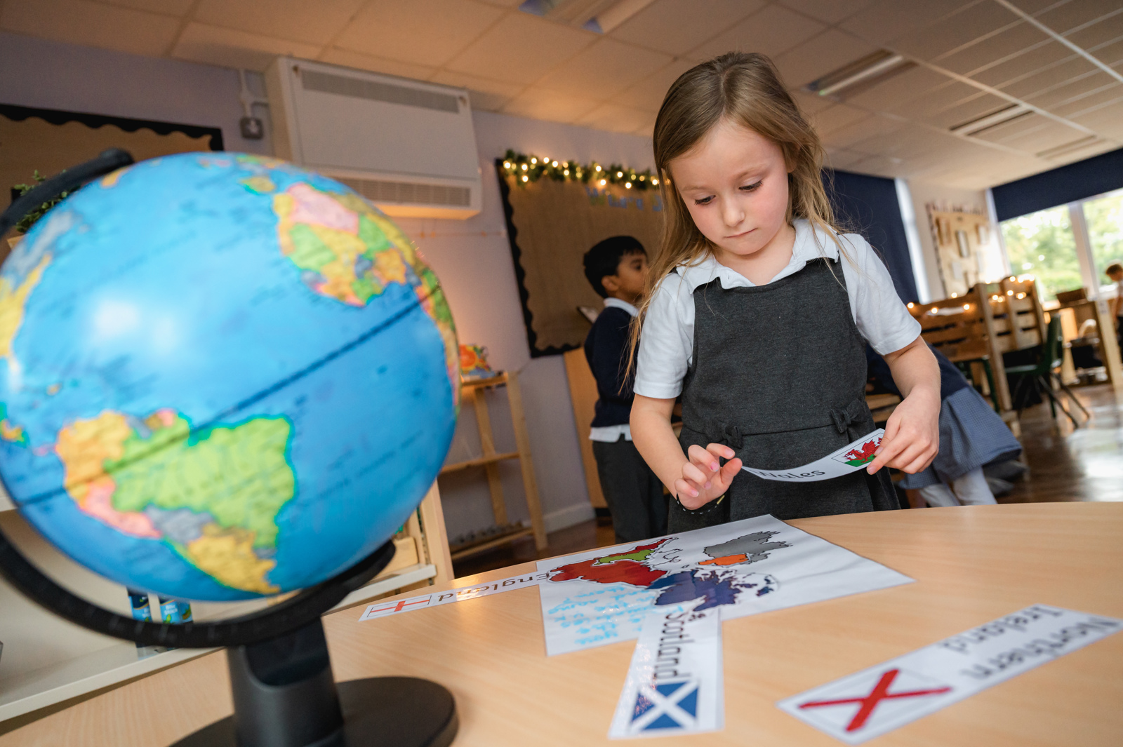 A year 1 girl matches flags of Great Britain with the corresponding areas of the country, a globe sits in the foreground.