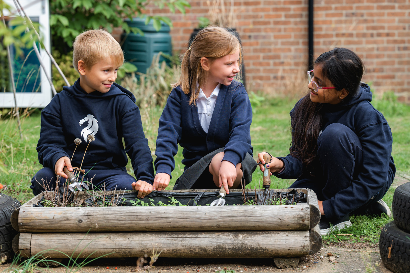 Children are using gardening tools to help with weeding in the allotment area